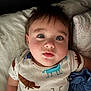 baby, child, onesie, animal_print, bed, pillow, blanket, face, eyes, hair, mouth, skin, infant, cute, lying_down, indoors, portrait, soft_lighting, expression, cozy