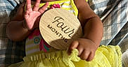 Emmalee joined the competition — help win amazing prizes! baby, smile, yellow_dress, wooden_sign, four_months, hand, face, blanket, pattern, infant, happy, lying_down, cute, clothing, child, portrait, celebration, milestone, small_hand, indoors