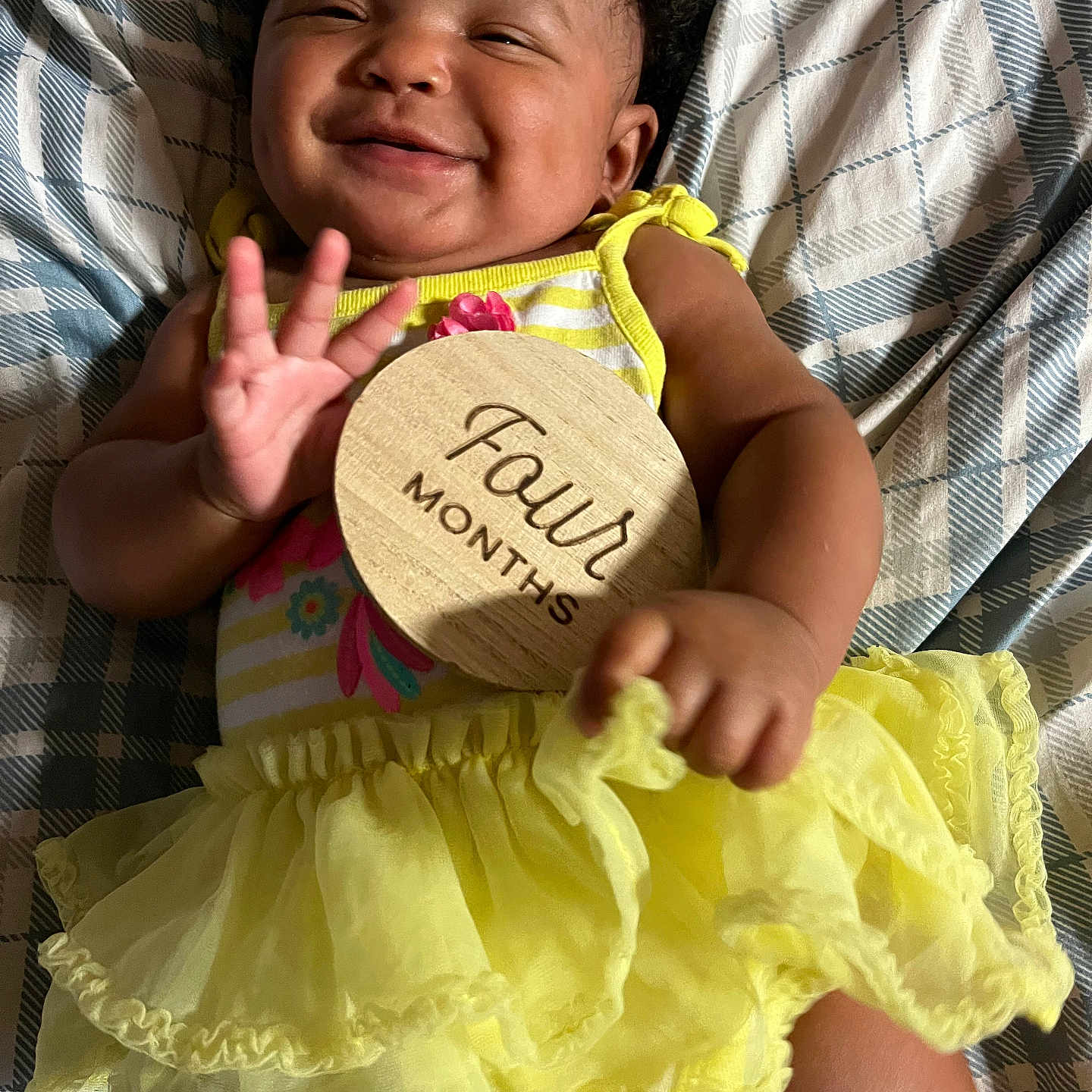 Emmalee joined the competition — help win amazing prizes! baby, smile, yellow_dress, wooden_sign, four_months, hand, face, blanket, pattern, infant, happy, lying_down, cute, clothing, child, portrait, celebration, milestone, small_hand, indoors