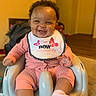 Emmalee is registered to the contest to win money with this photo: baby, child, smiling, bib, pink_clothing, curly_hair, baby_seat, indoor, happy, cute, person, infant, sitting, footwear, sock, face, expression, home, furniture, young_child