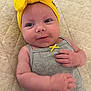 baby, infant, headband, yellow, bow, grey_outfit, cute, smiling, lying_down, pale_skin, hand, curious, closeup, indoors, quilted_surface, child, small_ribbon, soft_light, portrait, adorable