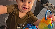 Ryder is registered to the contest to win money with this photo: baby, child, infant, smiling, happy, portrait, playpen, toy, rattle, colorful, indoor, sitting, standing, clothing, brown_shirt, camouflage_pants, face, eyes, playroom, household
