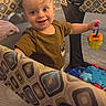 baby, child, toddler, smiling, happy, portrait, indoor, playpen, rattle, toy, infant, face, brown_hair, sitting, playtime, colorful, patterned_fabric, nursery, domestic_scene, photograph