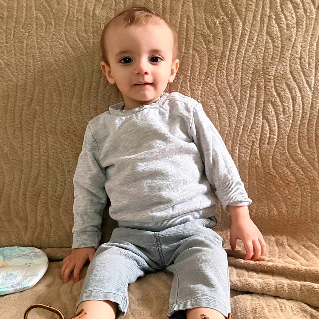 Carl participe au concours pour gagner de l'argent avec cette photo : toddler, child, sitting, couch, boots, footwear, indoors, clothing, beige, texture, casual, portrait, young_child, person, home, comfortable, neutral_expression, light_gray, cozy, baby