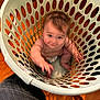 baby, child, laundry_basket, plastic, floor, wooden_floor, indoor, cute, infant, reaching, smiling, playful, sitting, diaper, skin, face, person, curious, home, furniture