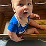 baby, child, drawer, wooden_furniture, blue_clothing, curious, sitting, indoors, face, eyes, hand, legs, floor, wood, onesie, infant, expression, cute, portrait, furniture