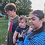 child, baby, girl, boy, outdoor, park, grass, tree, sunlight, curly_hair, holding, casual_clothing, blue_jacket, tshirt, people, daytime, nature, portrait, family, cute