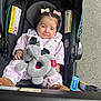 Isabella is registered to the contest to win money with this photo: baby, child, stroller, toy, elephant_toy, pink_clothing, hair_bows, pony_tail, brown_boots, seat_belt, outdoor, asphalt, car_seat, infant, cute, smiling, person, safety, comfort, portrait
