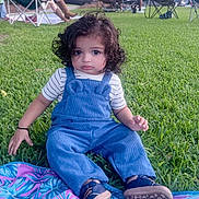 Atharv is registered to the contest to win money with this photo: child, toddler, curly_hair, portrait, sitting, outdoor, grass, lawn, picnic, blanket, colorful_blanket, blue_overalls, striped_shirt, shoes, sunset, park, folding_chairs, cars, trees, family_gathering