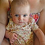baby, child, person, face, blue_eyes, floral_shirt, hand, arm, skin, sitting, close_up, indoor, holding, cute, infant, expression, human, portrait, young, parent