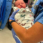 Alpha joined the competition — help win amazing prizes! newborn, baby, hospital, medical_staff, blue_gloves, blanket, footprints, scrubs, healthcare_worker, patient_care, infant, holding, indoor, medical_equipment, person, clinic, face, sleeping, close_up, care