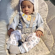 William is registered to the contest to win money with this photo: baby, child, infant, hat, pajamas, baby_seat, straps, cushion, patterned_clothing, socks, indoors, calm, cute, face, person, young_child, apparel, soft_texture, comfort, seated