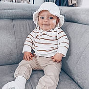 Tiago a rejoint le concours — aidez-le/la à gagner de superbes lots ! baby, casual_clothing, child, couch, cozy, cute, furniture, gray_furniture, happy, hat, home_interior, indoor, living_room, person, portrait, seated, smiling, socks, striped_clothing, young_child