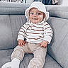 baby, casual_clothing, child, couch, cozy, cute, furniture, gray_furniture, happy, hat, home_interior, indoor, living_room, person, portrait, seated, smiling, socks, striped_clothing, young_child