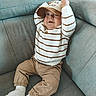 Tiago a rejoint le concours — aidez-le/la à gagner de superbes lots ! baby, beige_pants, cap, casual_clothing, child, comfortable, couch, cozy, cute, gray_couch, home_interior, indoor, person, playful, portrait, seated, striped_sweater, surprised_expression, white_socks, young_child