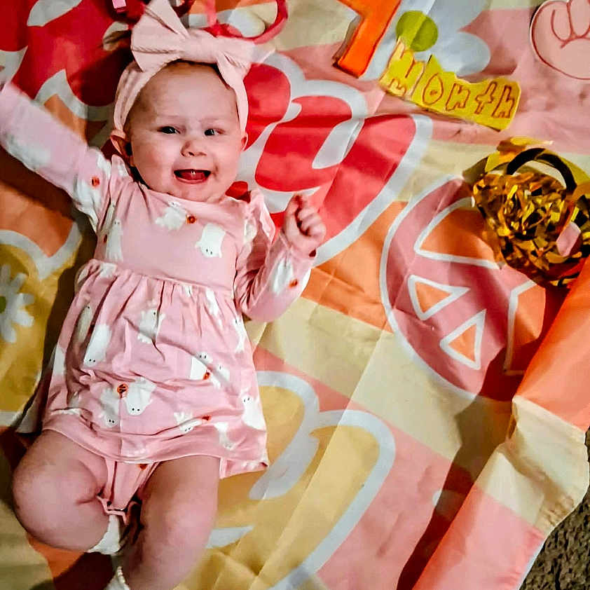 Blakely-Peach joined the competition — help win amazing prizes! baby, blanket, bow, child, colorful, dress, face, feet, hand, happy, indoor, infant, lying_down, patterned, photograph, pink_clothing, playtime, portrait, smiling, toy