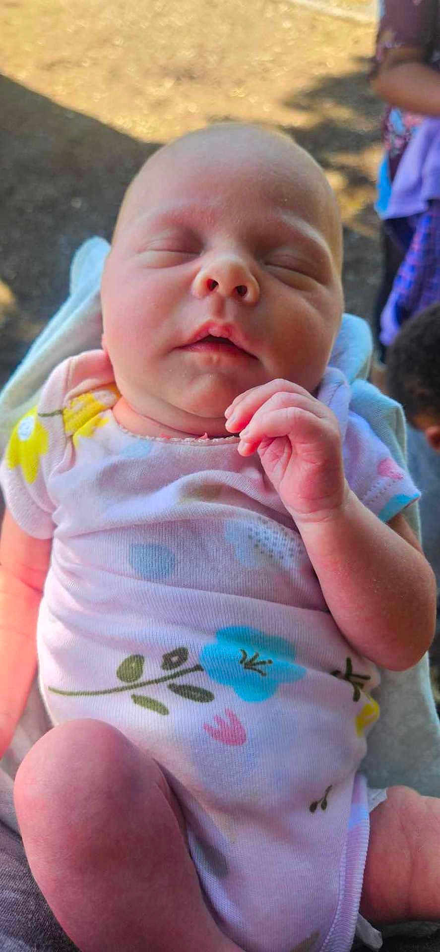 Leilani is registered to the contest to win money with this photo: baby, sleeping, infant, onesie, floral_pattern, hand, skin, outdoor, natural_light, peaceful, closeup, portrait, child, newborn, person, soft, background_blur, relaxation, cute, young