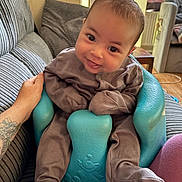 Arie joined the competition — help win amazing prizes! baby, smiling, infant, baby_seat, couch, striped_couch, tattoo, hand, indoors, living_room, cozy, brown_clothing, turquoise_seat, happy, child, person, footwear, seat, furniture, support