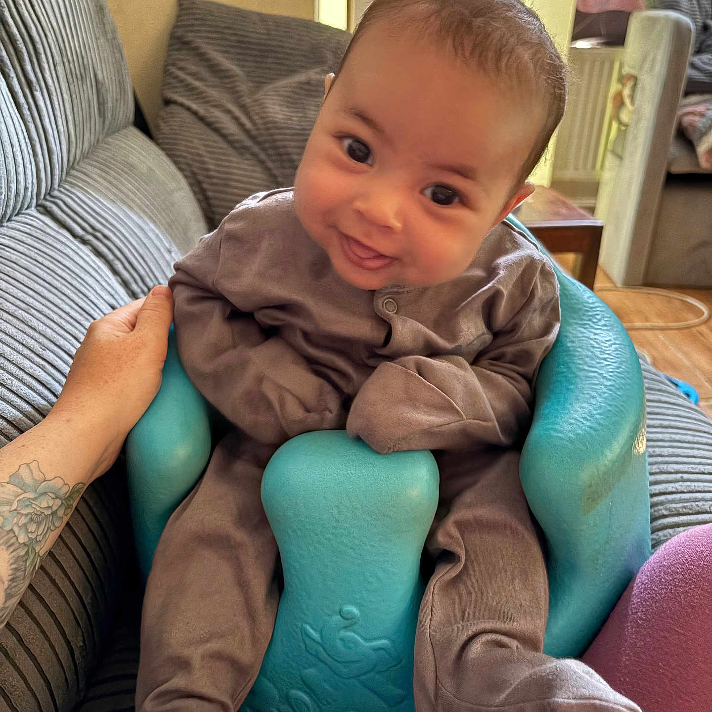 Arie joined the competition — help win amazing prizes! baby, baby_seat, brown_clothing, child, couch, cozy, footwear, furniture, hand, happy, indoors, infant, living_room, person, seat, smiling, striped_couch, support, tattoo, turquoise_seat