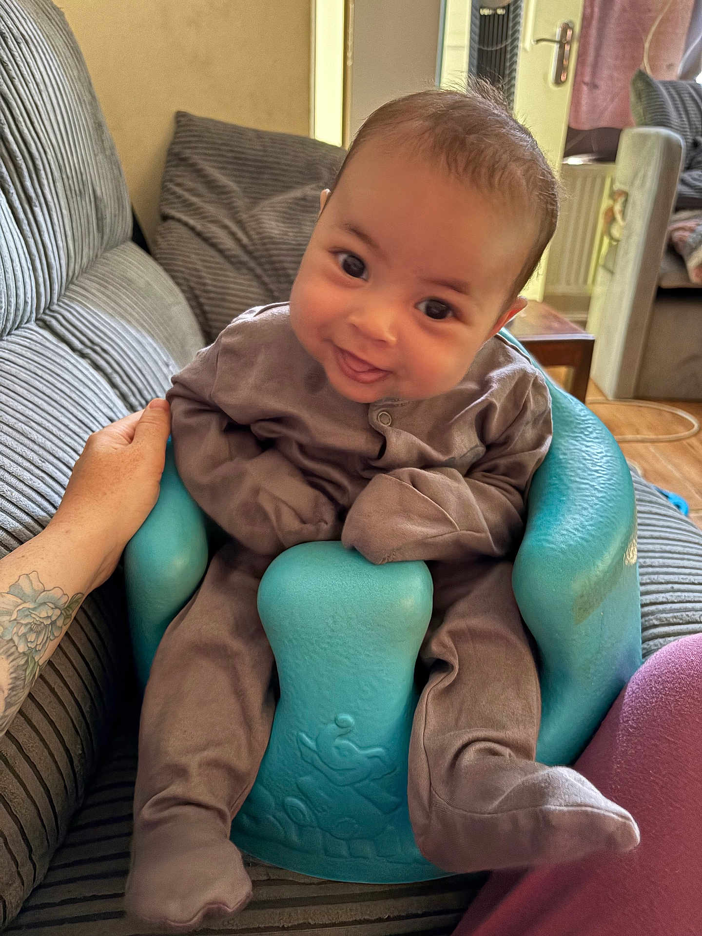Arie joined the competition — help win amazing prizes! baby, smiling, infant, baby_seat, couch, striped_couch, tattoo, hand, indoors, living_room, cozy, brown_clothing, turquoise_seat, happy, child, person, footwear, seat, furniture, support