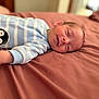 Crue joined the competition — help win amazing prizes! baby, newborn, infant, bed, blanket, sleeping, smiling, face, cozy, onesie, penguin_patch, blue_stripes, soft_light, closeup, portrait, child, peaceful, indoors, resting, cute