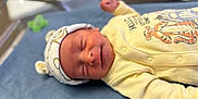 Crue is registered to the contest to win money with this photo: newborn, baby, sleeping, infant, yellow_onesie, hat, bear_ears, blue_blanket, hospital, bassinet, cute, peaceful, portrait, clothing, child, person, lying_down, soft_texture, closeup, smile
