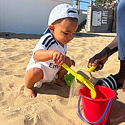 Adama participe au concours pour gagner de l'argent avec cette photo : adult_hand, beach, blue_sky, bucket, building, cap, child, footwear, fun, outdoor, people, playing, recreation, sand, shovel, summer, sunny, toddler, vacation, white_clothing