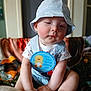 Sebastian is registered to the contest to win money with this photo: baby, child, sitting, hat, bucket_hat, overalls, badge, blanket, indoors, cute, infant, face, hands, legs, clothing, expression, room, soft_lighting, early_milestone, portrait