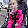 baby, child, stroller, pacifier, pink_clothing, bow, urban, street, car, pedestrian, face, infant, outdoor, cute, sitting, young_child, daylight, casual, people, transportation