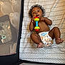 baby, infant, diaper, rattle, playpen, mattress, zigzag_pattern, curly_hair, bare_chest, child, toy, floor_bed, cute, small_feet, indoors, mesh_sides, baby_toy, lying_down, young_child, playtime