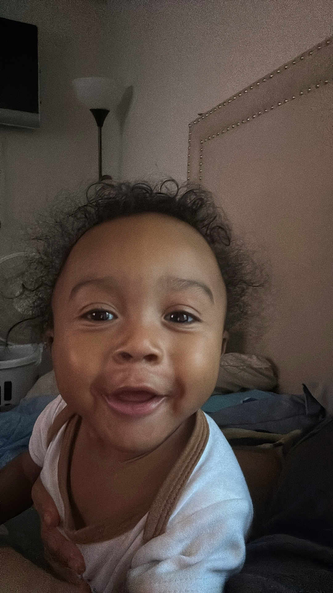 Sekani is registered to the contest to win money with this photo: baby, child, face, smile, curly_hair, indoor, bedroom, lamp, blanket, person, cute, infant, happy, portrait, clothing, head, young_child, closeup, expression, skin