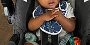 Sekani is registered to the contest to win money with this photo: baby, child, car_seat, safety_harness, bib, curly_hair, white_socks, toy, floor, wood_flooring, infant, seat_belt, expression, hands, clothing, indoor, warning_label, face, portrait, person
