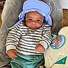baby, child, cap, striped_shirt, green_pants, mirror, plush_toy, blanket, indoor, face, portrait, smiling, hand, furniture, floor, reflection, cute, relaxed, person, cozy