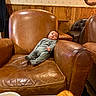 baby, infant, leather_chair, armchair, coffee, croissant, food, table, wood_paneling, wallpaper, portrait, photo_frame, cozy, indoor, seated, relaxed, clothing, person, cafe, snack