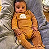 baby, infant, pajamas, blanket, pacifier, indoor, soft_texture, brown_clothing, cute, child, face, expression, comfort, plush, footed_pajamas, person, seated, warm_lighting, home, cozy
