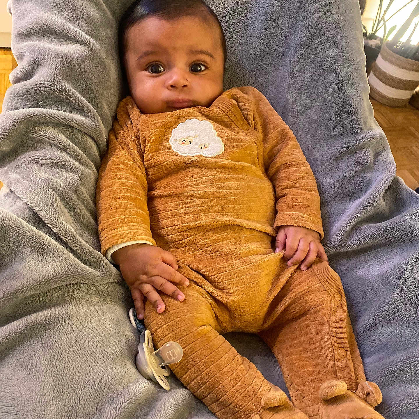 Raayan a rejoint le concours — aidez-le/la à gagner de superbes lots ! baby, infant, pajamas, blanket, pacifier, indoor, soft_texture, brown_clothing, cute, child, face, expression, comfort, plush, footed_pajamas, person, seated, warm_lighting, home, cozy