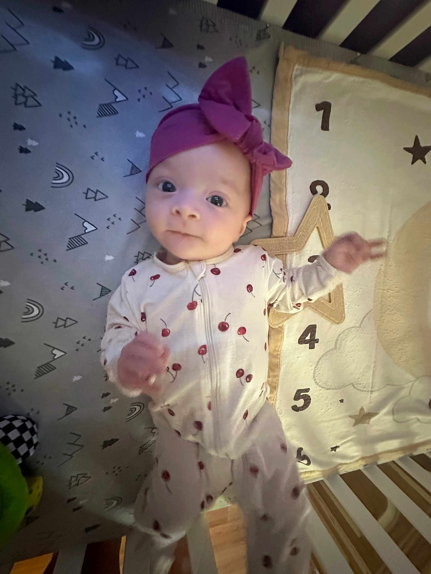 Rayna is registered to the contest to win money with this photo: baby, child, infant, onesie, headband, crib, bedding, pattern, cherry, purple, numbers, soft, cute, sleepwear, playful, curious, lying_down, indoors, person, young_child