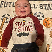 Ezra joined the competition — help win amazing prizes! baby, smiling, infant, clothing, blanket, sports, baseball, soccer_ball, basketball, mustache_graphic, shirt, cute, happy, lying_down, child, portrait, indoors, young_child, playful, face
