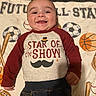 baby, smiling, infant, clothing, blanket, sports, baseball, soccer_ball, basketball, mustache_graphic, shirt, cute, happy, lying_down, child, portrait, indoors, young_child, playful, face
