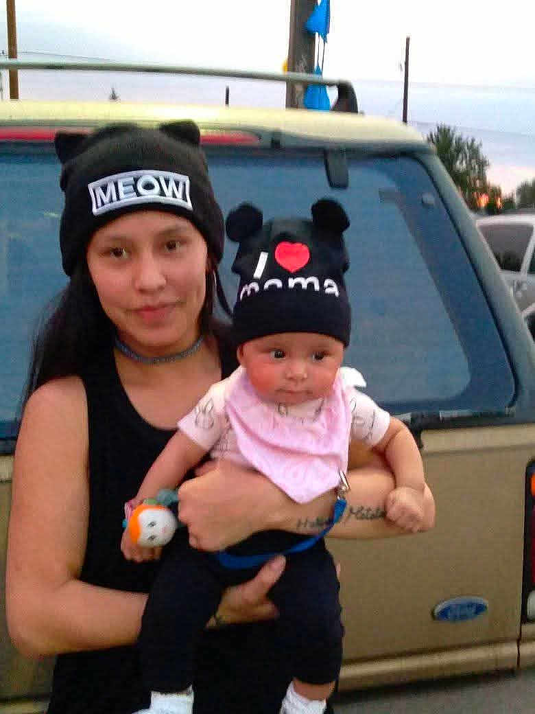 Nala is registered to the contest to win money with this photo: woman, baby, hat, black_hat, text_on_hat, outdoor, car, vehicle, person, child, holding, cute, dusk, casual_clothing, toy, pink_bib, smile, face, portrait, family