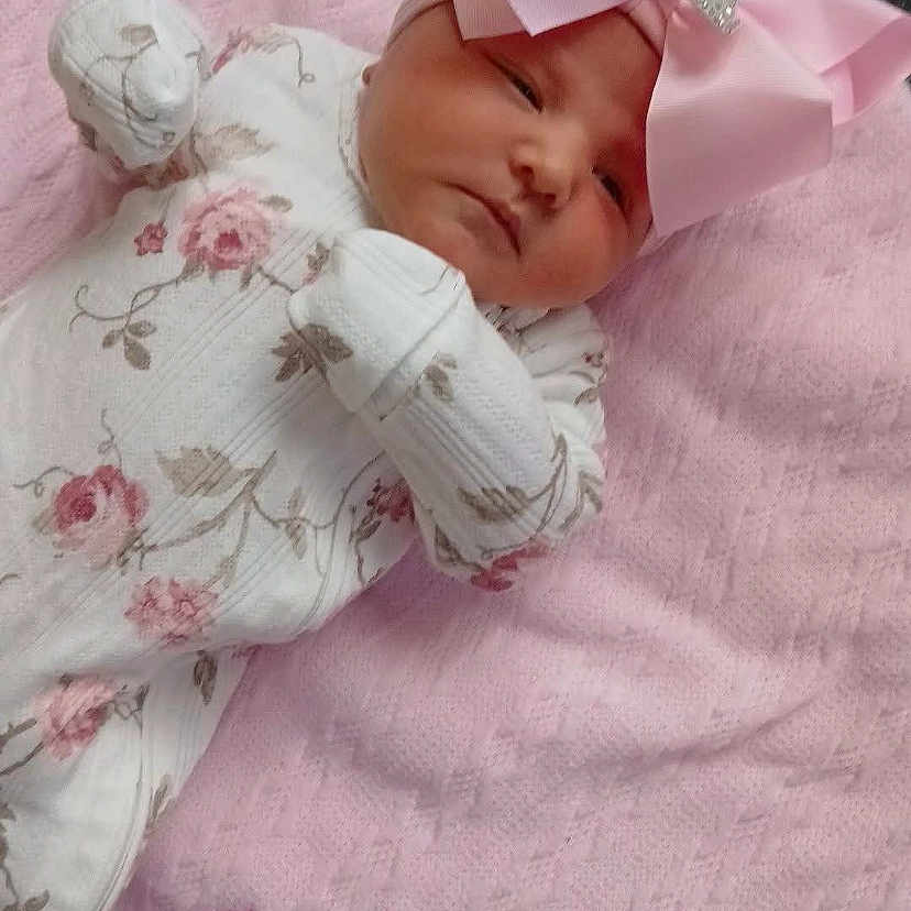 Amira Mae is registered to the contest to win money with this photo: baby, baby_clothes, blanket, child, cozy, cute, embroidered_text, floral_onesie, headband, indoor, infant, newborn, peaceful, pink, pink_bow, portrait, resting, sleepy, soft_texture, white