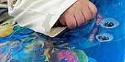 Bramh is registered to the contest to win money with this photo: baby, hand, fist, sleeve, clothing, play_mat, colorful, sea_creatures, water_bubbles, blue, yellow, pink, orange, green, infant, cute, pattern, soft_fabric, closeup, child