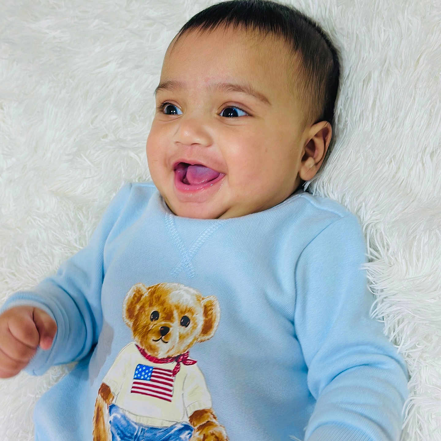 Bramh is registered to the contest to win money with this photo: american_flag, baby, blanket, blue_sweater, bright_eyes, child, clothing, cute, face, happy, indoors, infant, lying_down, open_mouth, person, portrait, smiling, soft_texture, teddy_bear, young_child