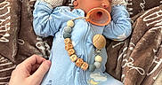 Waylon joined the competition — help win amazing prizes! baby, newborn, sleeping, blue_onesie, hat, mittens, pacifier, hand, blanket, brown_blanket, wooden_beads, clothing, infant, cute, peaceful, indoor, person, soft_texture, nap, resting
