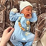 baby, newborn, sleeping, blue_onesie, hat, mittens, pacifier, hand, blanket, brown_blanket, wooden_beads, clothing, infant, cute, peaceful, indoor, person, soft_texture, nap, resting