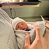 Waylon is registered to the contest to win money with this photo: newborn, baby, blanket, hat, hand, hospital, person, sleeping, indoor, clothing, bedside, cups, laptop, soft_light, rest, care, tenderness, infant, portrait, closeup