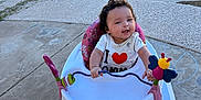 Audrina is registered to the contest to win money with this photo: baby, baby_walker, child, smiling, outdoor, concrete, pool, empty_pool, toy, pink, white, shirt, heart, happy, person, playful, sunlight, grass, sidewalk, clothing