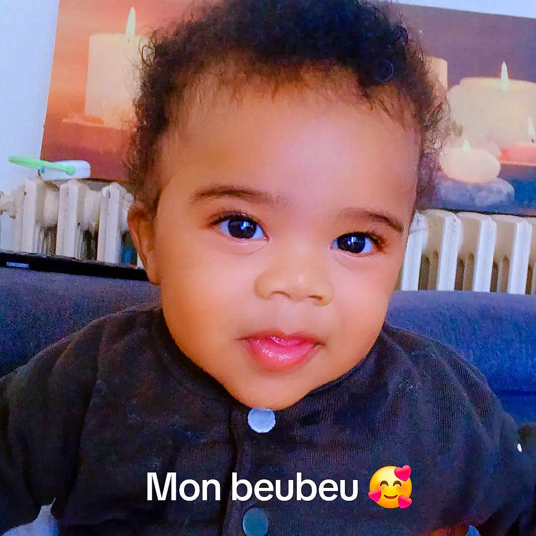 émile-Lamine participe au concours pour gagner de l'argent avec cette photo : baby, child, indoor, portrait, smile, curly_hair, sweater, pants, radiator, candle, hand, person, cute, face, seated, cozy, expression, infant, warm, background