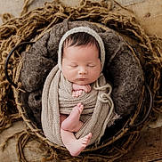 Layne is registered to the contest to win money with this photo: newborn, baby, sleeping, basket, blanket, knit, wrapped, cozy, soft, infant, peaceful, resting, wooden_floor, brown, beige, texture, cute, portrait, headwear, fingers