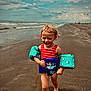 child, toddler, beach, water, ocean, sand, swimsuit, floaties, barefoot, happy, running, cloudy_sky, waves, summer, vacation, outdoor, fun, play, water_toys, smile
